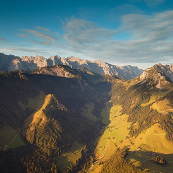 Vogelblick auf die atemberaubenden, sonnengetränkten Berge in Tirol unter leicht bewölktem Himmel.