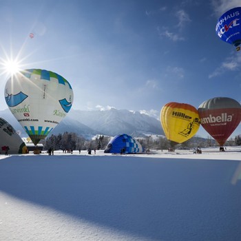 Zahlreiche bunte Heißluftballons heben nach der Reihe von schneebedeckten Feld ab.